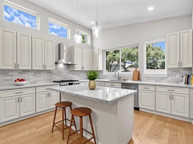 6100 Duplessis St, New Orleans, LA 70122 - kitchen with wall chimney range hood, stainless steel dishwasher, white cabinetry, tasteful backsplash, and decorative light fixtures