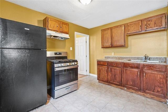 3309 4th St, New Orleans, LA 70125 - kitchen with freestanding refrigerator, gas stove, under cabinet range hood, a sink, and brown cabinetry