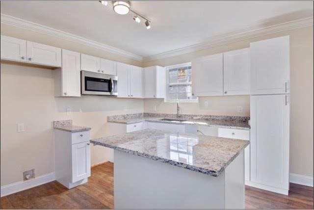 921 Andry St, New Orleans, LA 70117 - kitchen with stainless steel microwave, white cabinets, light stone counters, a sink, and dark wood finished floors