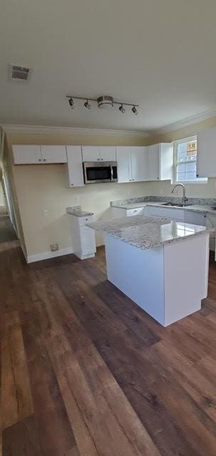 921 Andry St, New Orleans, LA 70117 - kitchen with stainless steel microwave, a sink, white cabinets, dark wood-style floors, and ornamental molding