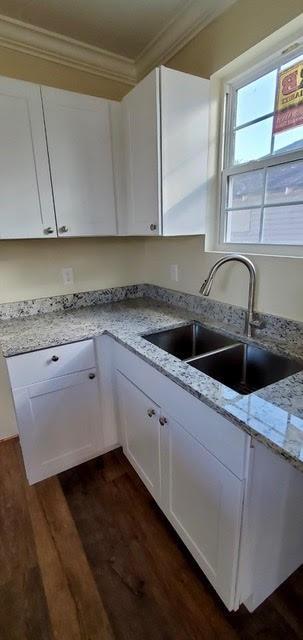 921 Andry St, New Orleans, LA 70117 - kitchen featuring a sink, ornamental molding, dark wood-style flooring, white cabinets, and light stone countertops