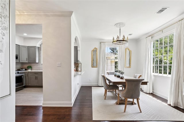 6951 Memphis St, New Orleans, LA 70124 - dining area featuring arched walkways, ornamental molding, baseboards, a chandelier, and dark wood-style floors