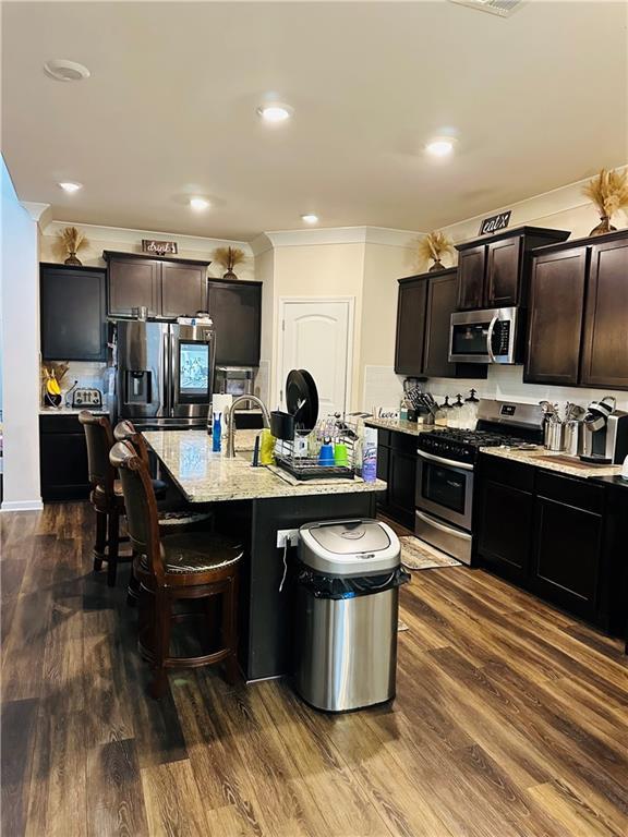 1393 Shipyard Dr, Slidell, LA 70461 - kitchen with appliances with stainless steel finishes, ornamental molding, a breakfast bar, dark wood finished floors, and a kitchen island with sink
