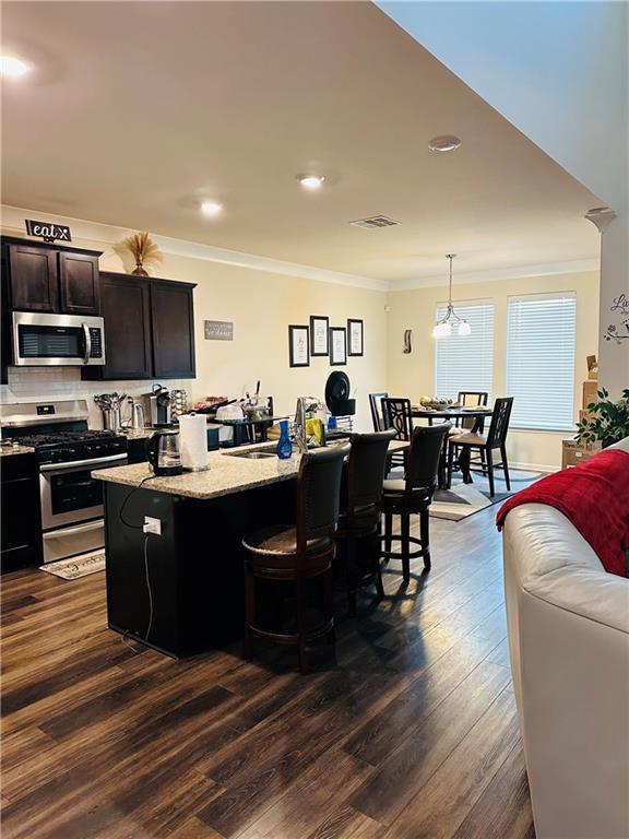 1393 Shipyard Dr, Slidell, LA 70461 - kitchen with stainless steel appliances, crown molding, a kitchen island with sink, dark wood finished floors, and a breakfast bar area