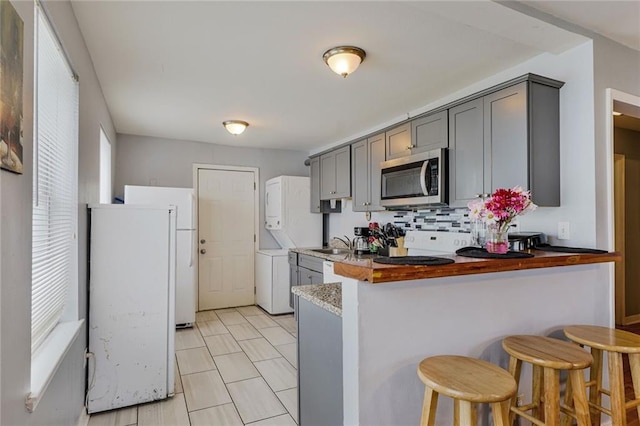 6223 Wainwright Dr, New Orleans, LA 70122 - kitchen with stainless steel microwave, gray cabinets, a peninsula, and stacked washing machine and dryer