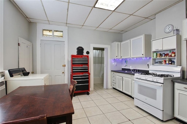 232830 Frenchmen St, New Orleans, LA 70119 - kitchen featuring white range with gas stovetop, dark countertops, washer and clothes dryer, light tile patterned floors, and a drop ceiling