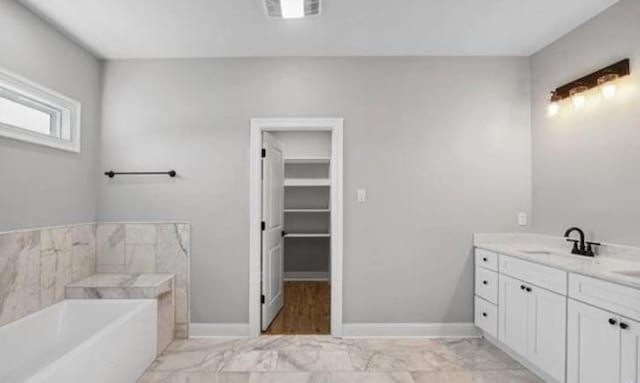220 Trudeau Dr, Metairie, LA 70003 - bathroom featuring vanity, marble look tile flooring, a garden tub, a walk in closet, and baseboards