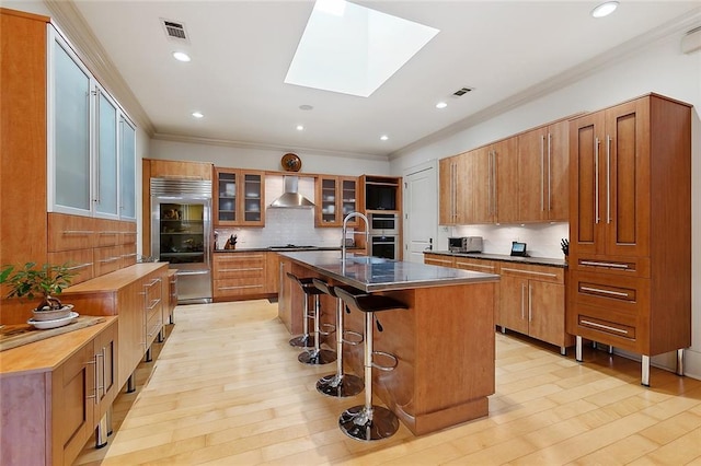 109 Northline St, Metairie, LA 70005 - kitchen with wall chimney range hood, built in fridge, brown cabinets, a skylight, and backsplash