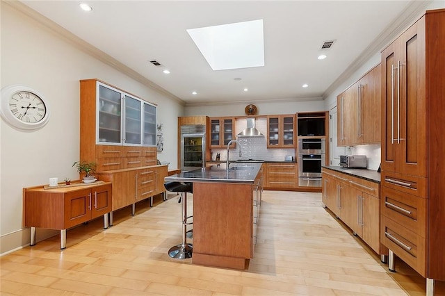 109 Northline St, Metairie, LA 70005 - kitchen featuring wall chimney exhaust hood, a skylight, dark countertops, tasteful backsplash, and a breakfast bar