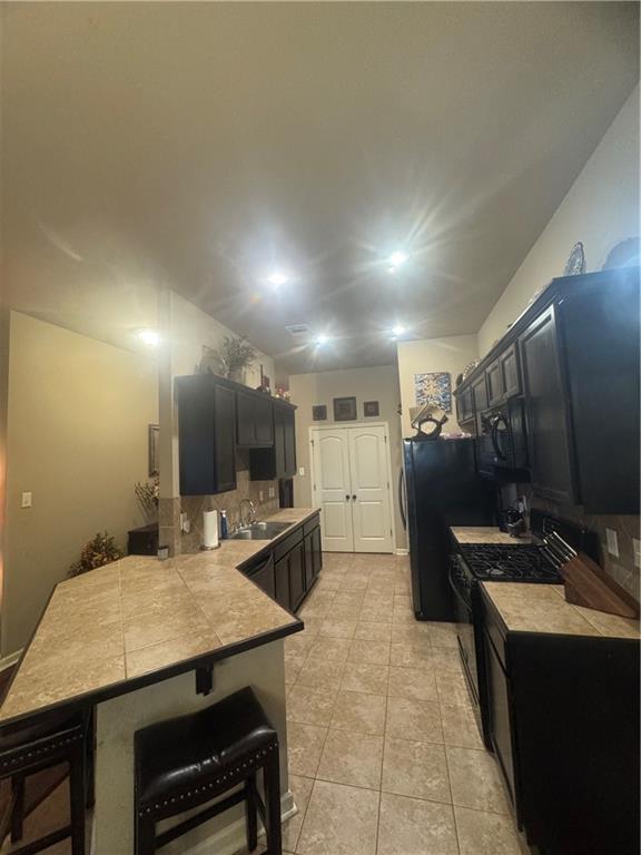 11018 Regency Ave, Hammond, LA 70403 - kitchen featuring backsplash, dark cabinetry, black appliances, and a kitchen breakfast bar