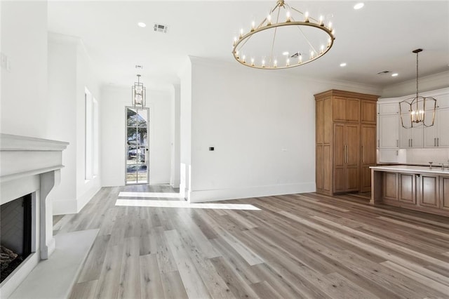 1001 Helios Ave, Metairie, LA 70005 - unfurnished dining area featuring a chandelier, light wood-type flooring, a fireplace with raised hearth, baseboards, and crown molding