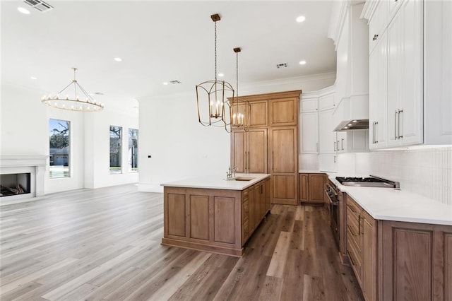1001 Helios Ave, Metairie, LA 70005 - kitchen with a chandelier, an island with sink, custom exhaust hood, light wood-style flooring, and crown molding