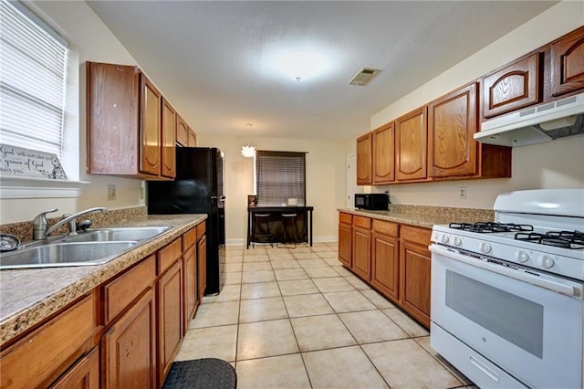 7701 Allison Rd, New Orleans, LA 70126 - kitchen featuring gas range gas stove, a sink, under cabinet range hood, freestanding refrigerator, and brown cabinetry