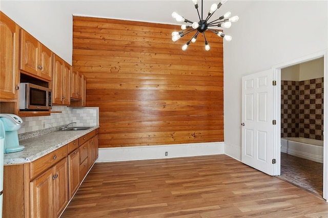1314 Ursulines Ave, New Orleans, LA 70116 - kitchen with stainless steel microwave, a chandelier, tasteful backsplash, brown cabinets, and light wood-type flooring