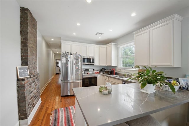 491113 Willow St, New Orleans, LA 70115 - kitchen with stainless steel appliances, a peninsula, a sink, light wood-style flooring, and white cabinets
