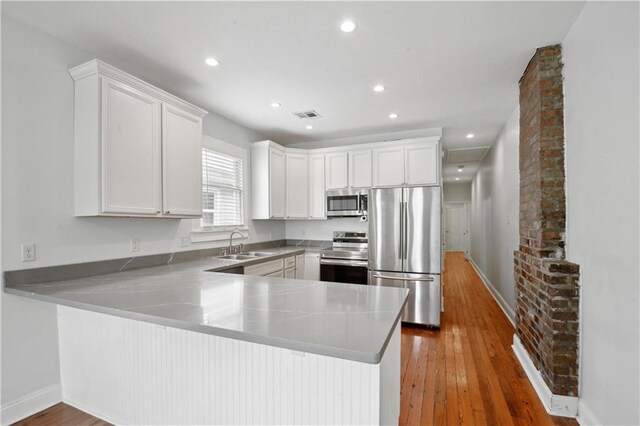 491113 Willow St, New Orleans, LA 70115 - kitchen featuring stainless steel appliances, a sink, a peninsula, white cabinets, and hardwood / wood-style flooring