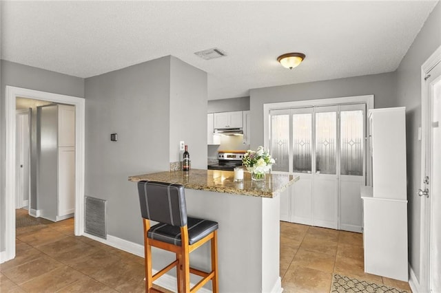 6020 Loraine St, Metairie, LA 70003 - kitchen with stainless steel range with electric stovetop, a breakfast bar area, white cabinetry, dark stone counters, and under cabinet range hood
