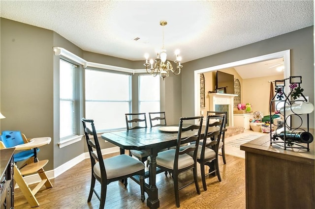21360 Stire St, Abita Springs, LA 70420 - dining area with light wood-style floors, a textured ceiling, a chandelier, baseboards, and a fireplace with raised hearth