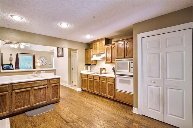 21360 Stire St, Abita Springs, LA 70420 - kitchen with white appliances, brown cabinetry, under cabinet range hood, a textured ceiling, and light countertops