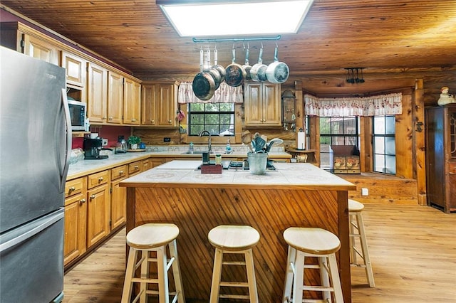 138 Ned Ave, Slidell, LA 70460 - kitchen featuring appliances with stainless steel finishes, a kitchen island, light wood-type flooring, tile counters, and a breakfast bar