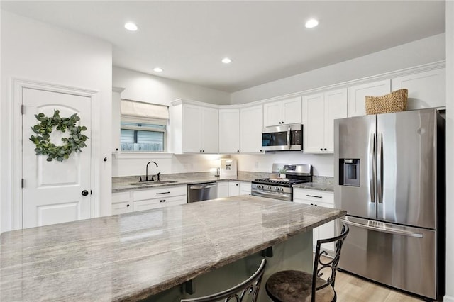 11557 Woodbluff Dr, Covington, LA 70433 - kitchen with stainless steel appliances, a sink, white cabinets, a kitchen breakfast bar, and light stone counters