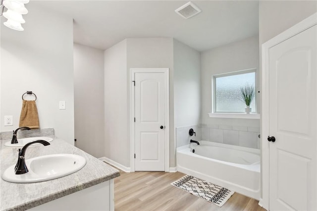 11557 Woodbluff Dr, Covington, LA 70433 - bathroom featuring a garden tub, wood finished floors, double vanity, and baseboards