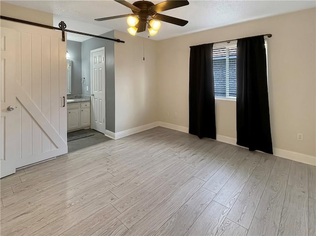 128 Hollowrock Ct, Slidell, LA 70461 - unfurnished bedroom with a barn door, light wood finished floors, baseboards, connected bathroom, and a ceiling fan
