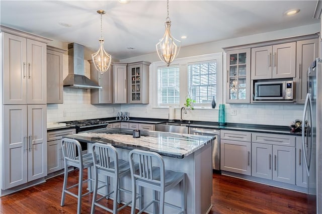 2134 Harmony St, New Orleans, LA 70115 - kitchen featuring wall chimney exhaust hood, gray cabinetry, appliances with stainless steel finishes, a sink, and a chandelier