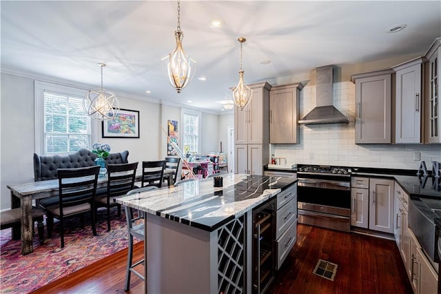 2134 Harmony St, New Orleans, LA 70115 - kitchen with wall chimney range hood, gray cabinetry, stainless steel gas range oven, a chandelier, and dark wood-style flooring