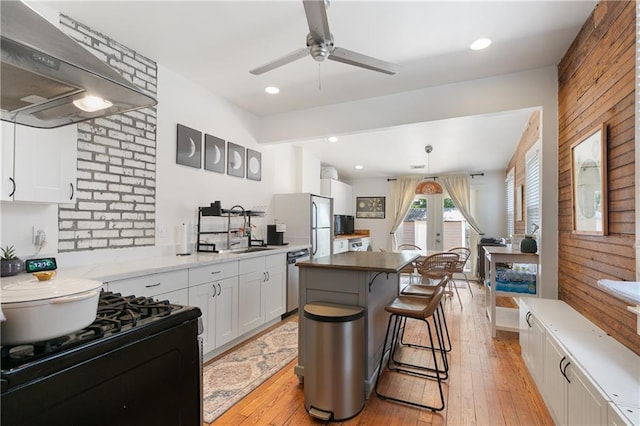 182527 Cambronne St, New Orleans, LA 70118 - kitchen with black gas range oven, a ceiling fan, under cabinet range hood, a kitchen breakfast bar, and white cabinetry