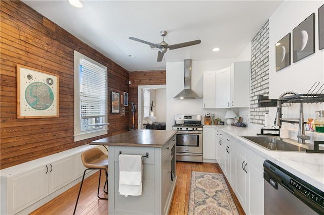 182527 Cambronne St, New Orleans, LA 70118 - kitchen with appliances with stainless steel finishes, a sink, wall chimney range hood, a ceiling fan, and light wood finished floors