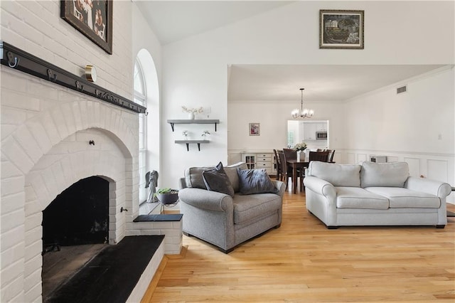 733 Plantation Dr, Abita Springs, LA 70420 - living room featuring a chandelier, light wood-style flooring, a brick fireplace, and high vaulted ceiling