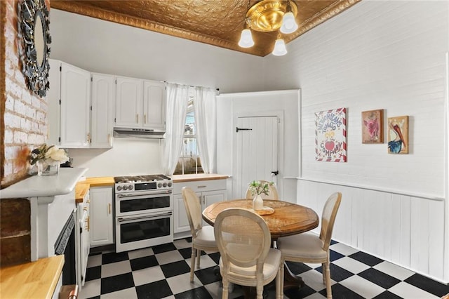 2728 Bell St, New Orleans, LA 70119 - kitchen with double oven range, dark floors, under cabinet range hood, white cabinetry, and an ornate ceiling