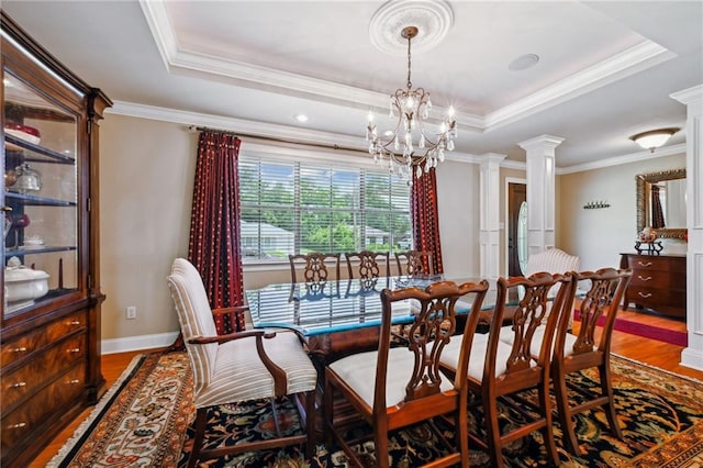 3845 Croydon St, Slidell, LA 70458 - dining area with wood finished floors, a tray ceiling, a chandelier, crown molding, and decorative columns