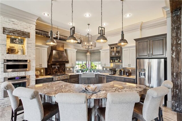 500 Tallow Tree Dr, Madisonville, LA 70447 - kitchen with premium range hood, light stone countertops, a sink, decorative backsplash, and ornamental molding