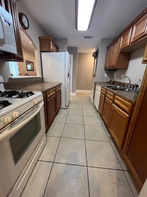 5917 Campus Blvd, New Orleans, LA 70126 - kitchen featuring white appliances, dark countertops, a sink, arched walkways, and light tile patterned floors