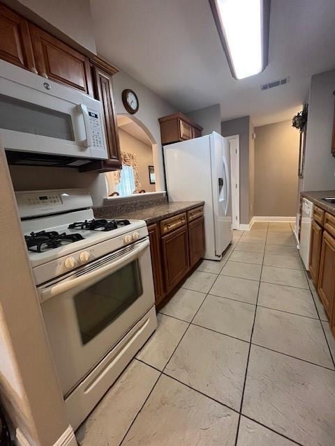 5917 Campus Blvd, New Orleans, LA 70126 - kitchen with white appliances, light tile patterned floors, dark countertops, baseboards, and arched walkways