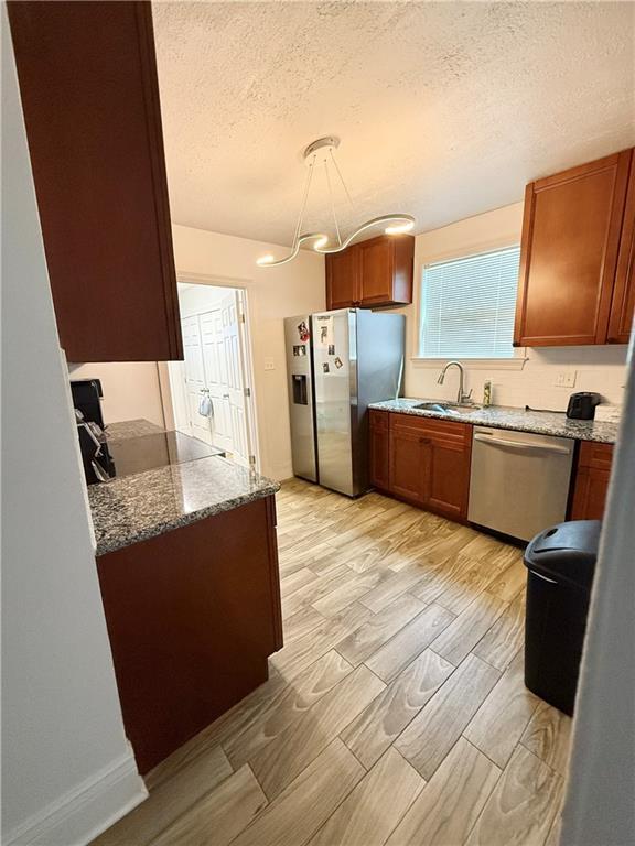 2012 Walkers Ln, Meraux, LA 70075 - kitchen featuring stainless steel appliances, a sink, a textured ceiling, stone countertops, and wood tiled floors