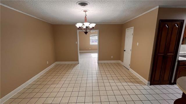 2008 Bluebird St, Slidell, LA 70460 - empty room with ornamental molding, a textured ceiling, a chandelier, light tile patterned floors, and baseboards