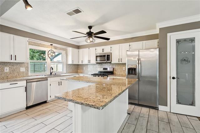 312 Raleigh Dr, Slidell, LA 70460 - kitchen with stainless steel appliances, light wood finished floors, white cabinets, and crown molding