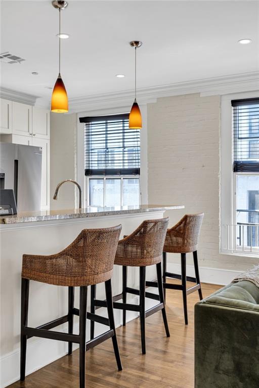 220 Decatur St Unit 302, New Orleans, LA 70130 - kitchen with fridge, crown molding, light wood finished floors, decorative light fixtures, and a kitchen bar