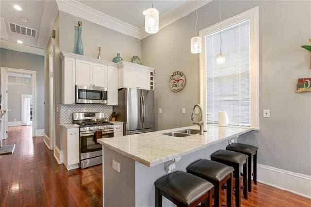 1355 Columbus St, New Orleans, LA 70116 - kitchen with stainless steel appliances, dark wood-type flooring, a breakfast bar area, white cabinetry, and backsplash