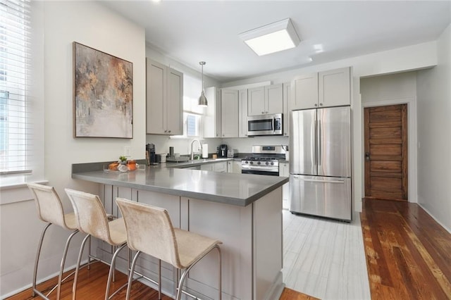 304 Henry Clay Ave, New Orleans, LA 70118 - kitchen featuring stainless steel appliances, a peninsula, gray cabinets, a kitchen bar, and wood finished floors