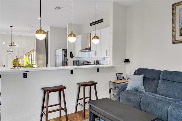 1039 Verret St, New Orleans, LA 70114 - kitchen with open floor plan, appliances with stainless steel finishes, a breakfast bar, wall chimney exhaust hood, and white cabinets