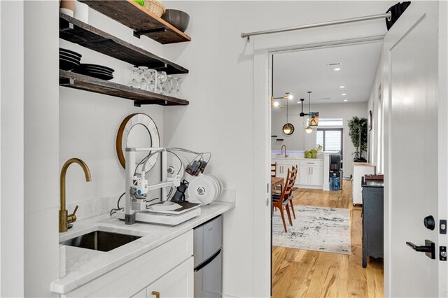 1039 Verret St, New Orleans, LA 70114 - kitchen featuring a sink, light wood-style flooring, white cabinetry, open shelves, and light stone counters