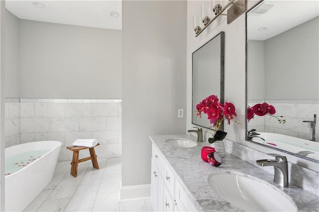 1827-29 Frenchmen St, New Orleans, LA 70116 - bathroom with double vanity, a soaking tub, marble look tiles, tile walls, and wainscoting