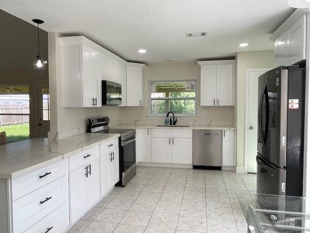 2120 Killington Dr, Harvey, LA 70058 - kitchen with stainless steel appliances, white cabinets, a peninsula, light stone countertops, and decorative light fixtures