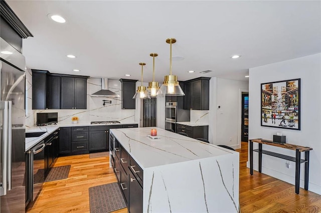 231 Audubon Blvd, New Orleans, LA 70125 - kitchen with wall chimney exhaust hood, stainless steel appliances, a center island, dark cabinetry, and light wood-type flooring