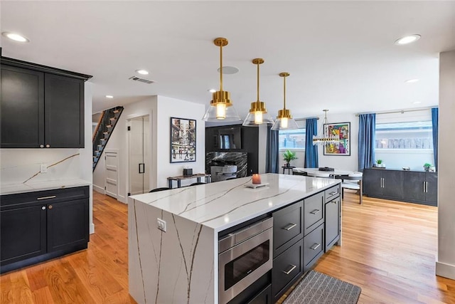 231 Audubon Blvd, New Orleans, LA 70125 - kitchen featuring stainless steel microwave, light wood-type flooring, a kitchen island, light stone counters, and decorative light fixtures