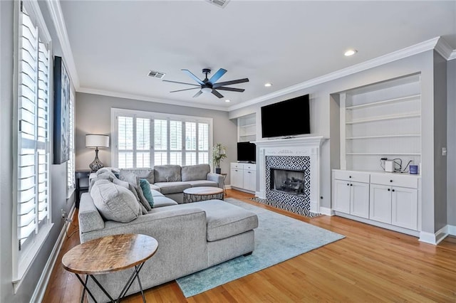 231 Audubon Blvd, New Orleans, LA 70125 - living room featuring a ceiling fan, light wood-style flooring, crown molding, a fireplace, and built in shelves